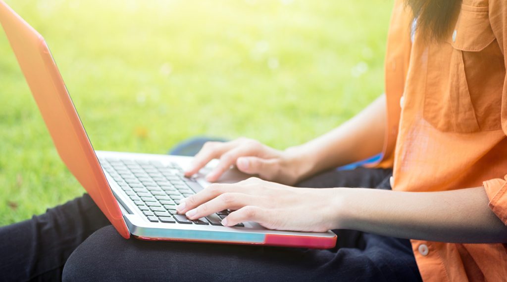 Young woman using computer on green glasses in the park. Education learning or freelance working outdoor or relaxation concept idea background.