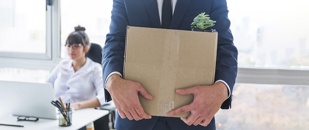 Close up of a man carrying his belongs out of the office in a cardboard box.