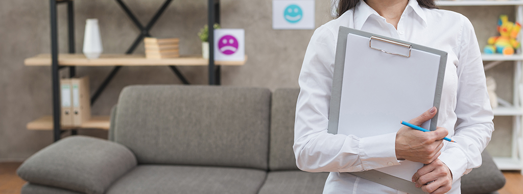 Psychologist standing in office holding clipboard and pencil.