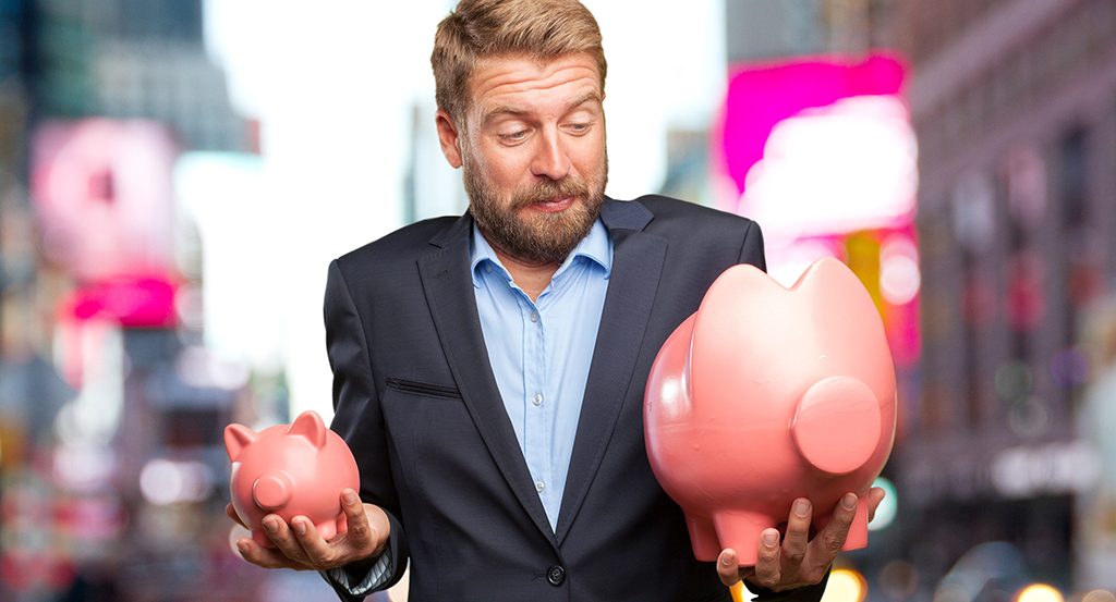 blond businessman holding one small piggy bank and one much larger piggy bank