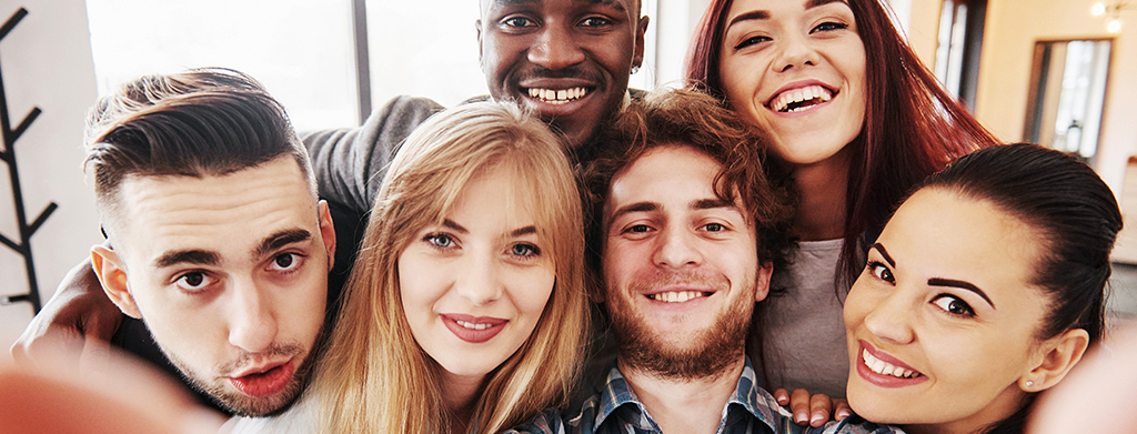 Teens having fun at restaurant. Three boys and three girls taking group selfie and laughing.