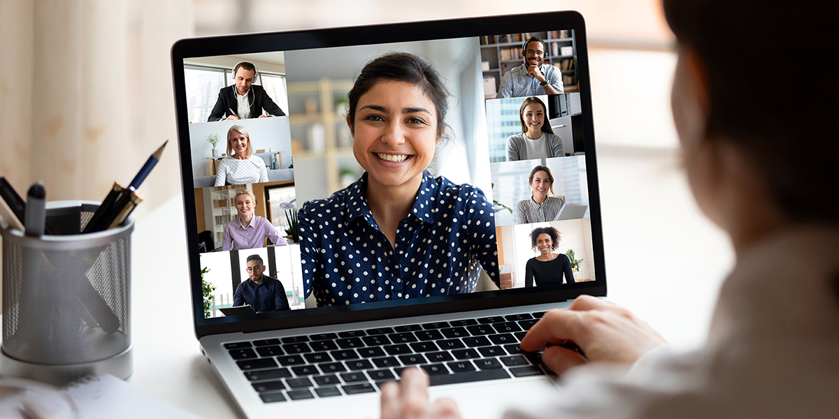 Woman sit at desk looking at computer screen where collage of diverse people webcam view. Indian ethnicity young woman lead video call distant chat, group of different mates using videoconference app.